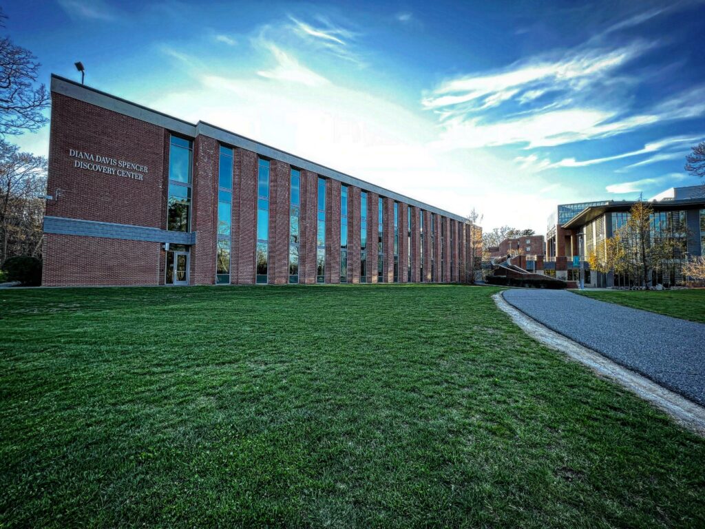 Long brick academic building with a blue sky and green grass in front of it. Sign on the building reads Diana Davis Spencer Discovery Center. 